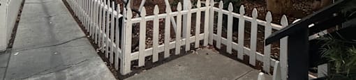 A white picket fence runs along the side of a concrete path.