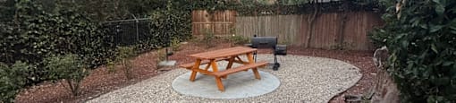A backyard with a picnic table and a gravel area.
