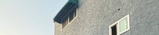 A grey building with a green dumpster in front of it.