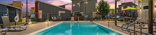 A large outdoor swimming pool with a sunset sky in the background.