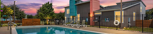 A swimming pool in front of a building with a sunset in the background.