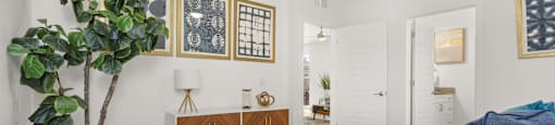 A bedroom with a large bed, a potted plant, and pictures on the wall.
