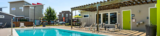 A large swimming pool with a wooden deck and sunshades.