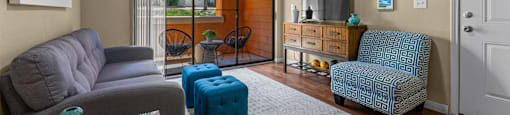 A living room with a grey couch, a blue ottoman, a green vase, and a painting on the wall.