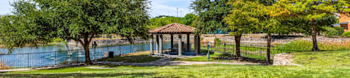 A gazebo sits in a grassy field next to a lake.