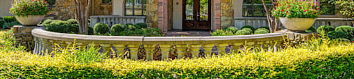 A house with a stone facade and a brown door is surrounded by a garden with yellow flowers.