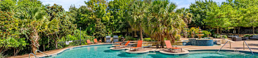 A large outdoor swimming pool surrounded by trees and lounge chairs.