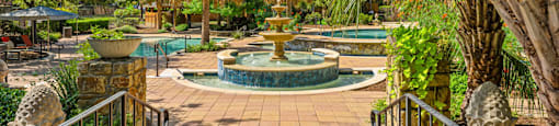 A beautiful outdoor pool area with a fountain in the middle.