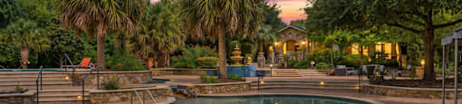 A swimming pool surrounded by palm trees and a stone wall.