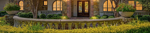A house with a stone facade and a large front yard with a variety of flowers.