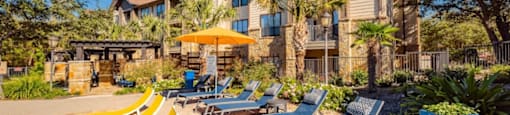 A sunny day at a resort with yellow sun loungers and a pool.