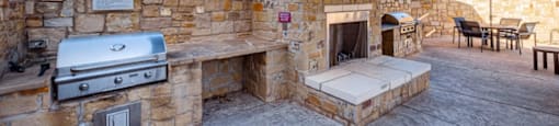 A stone patio with a grill and a fireplace.