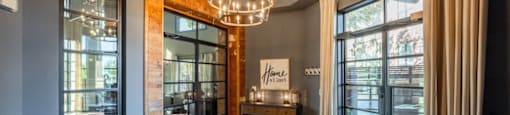 A room with a chandelier, a table with a sign that says "home" on it, and a view of the outside through the windows.
