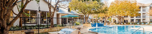 A poolside area with a stone grill and a tree in the foreground.