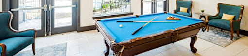A pool table is in the middle of a room with a chair and a couch.