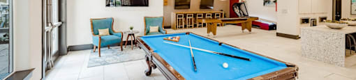 A pool table is in the middle of a room with a bar and a television.
