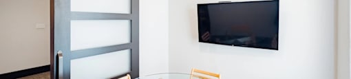 A glass table with four chairs and a television on the wall.