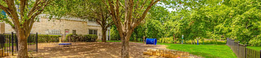 A red bench sits in a park with trees and a playground in the background.