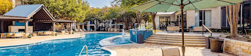 A pool area with a table and chairs and a green umbrella.