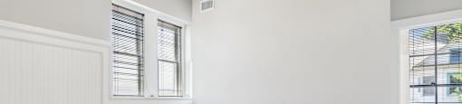 an empty bedroom with two windows and white walls