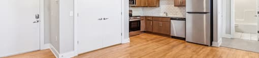 an empty kitchen with wood flooring and a stainless steel refrigerator