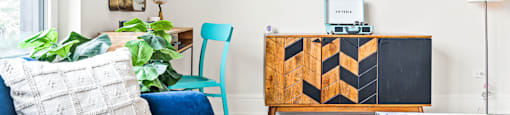 A blue couch with a white pillow and a wooden cabinet with a blackboard on it.