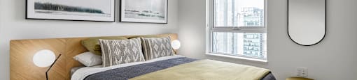 A bedroom with a bed, a nightstand with a lamp, and two pictures on the wall.