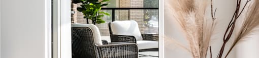 A living room with a grey round ottoman and a white vase with dried plants.