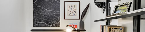 A black and white photo is on the wall above a desk with a chair and a table lamp.