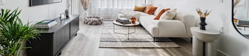 A modern living room with a white sofa, a wooden floor, and a large mirror on the wall.