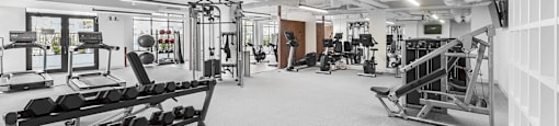 A gym with a variety of equipment including dumbbells, weight machines, and a bench press.