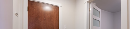 an empty room with a wooden door and a hallway with a white wall and a