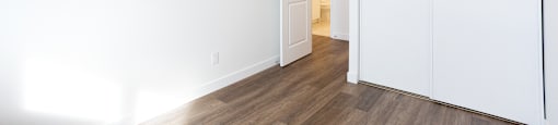 A room with white walls and wooden flooring with a white door.