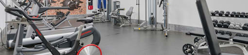 A gym with a variety of equipment including a stationary bike, a leg press machine, and a bench press.