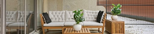 A patio with a white couch, wooden coffee table, and potted plants.