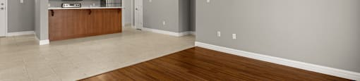A spacious room with wooden flooring and a kitchen area in the background.