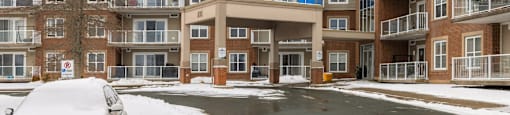 A car is parked in front of a building with a snowy tree.