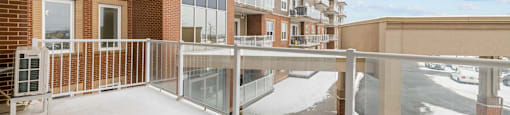 A snow-covered balcony with a glass railing and a building in the background.