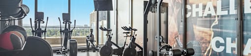 a gym with cardio equipment and a window view of the city