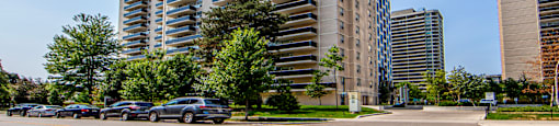 A tall residential building with a parking lot in front.