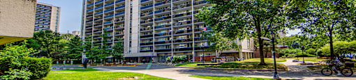 A tall building with many windows is surrounded by trees and greenery.