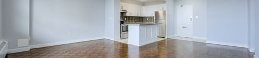 A large empty room with wooden flooring and white walls.