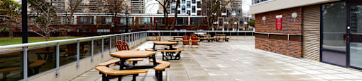 A patio with tables and benches is surrounded by buildings.