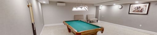 A room with a pool table and chairs.