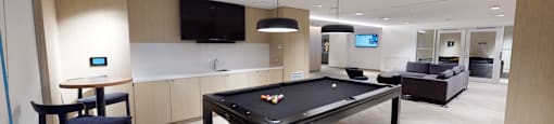 A pool table is in the middle of a room with a bar and a television.