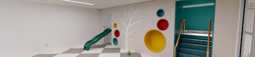 A play area with a slide and a tree design on the wall.