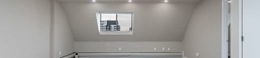A large empty room with a window and carpeted floor.
