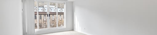 A room with a carpeted floor and a view of a building through a window.