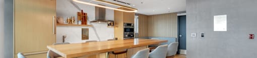 A modern kitchen with a long wooden island and blue chairs.