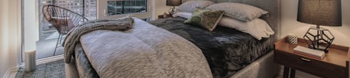 A bedroom with a large bed and a city view through the window.